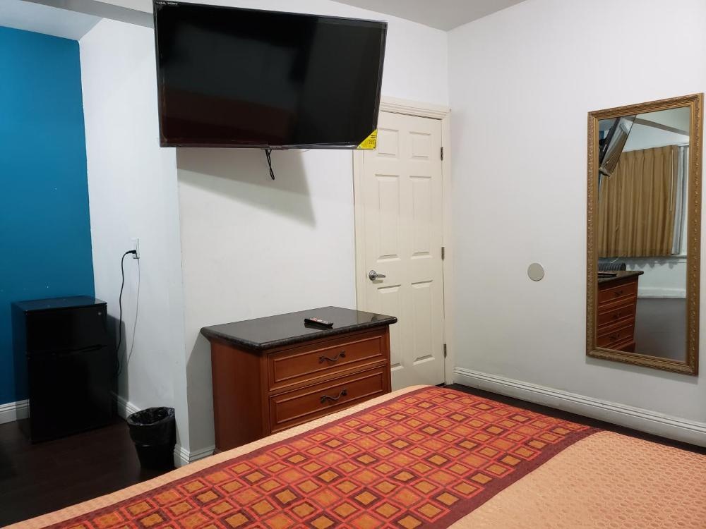 A hotel room with a bed, TV, mirror, nightstand, and refrigerator.