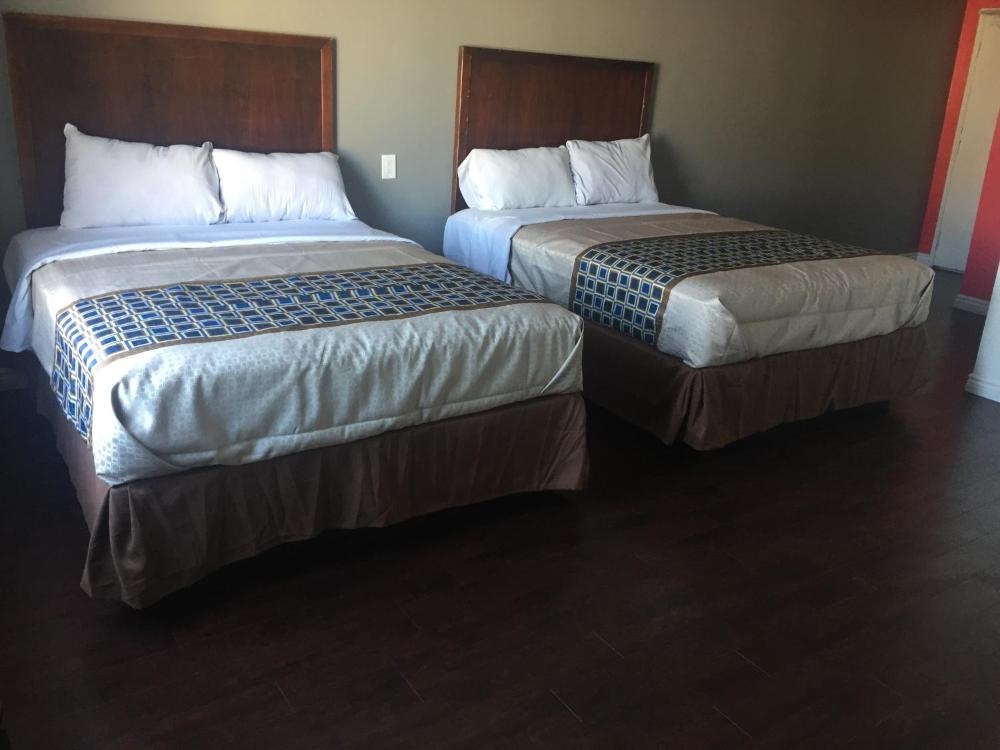 A hotel room with two beds, each with a wooden headboard, white pillows, and a brown and blue bedspread.